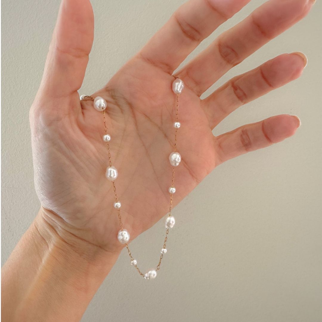 Pearl necklace draped over a hand against a neutral background