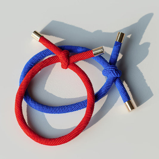 Red and blue braided hair ties with gold connectors on a light gray background