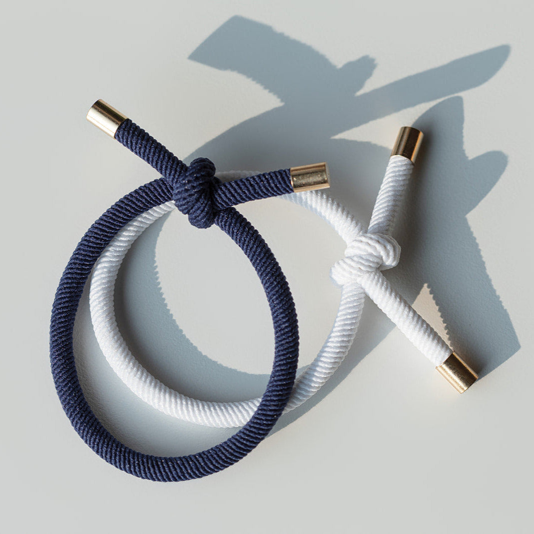 Navy and white hair ties with gold ends on a light gray background