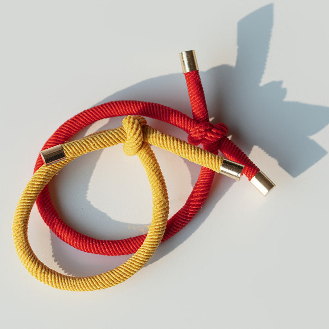 Two braided hair ties, one red and one yellow, on a light gray background.