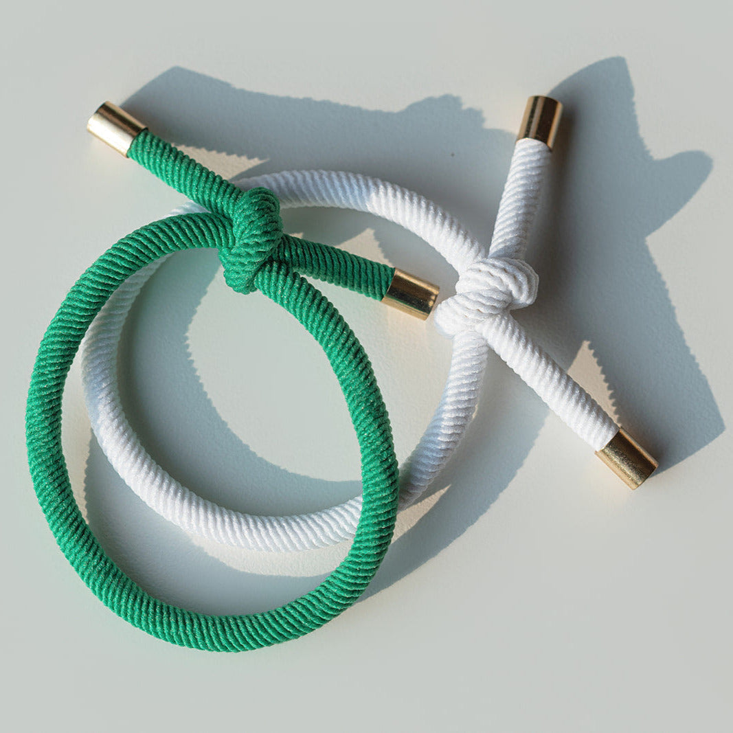 Two braided hair ties, one green and one white, with gold ends on a light gray background.