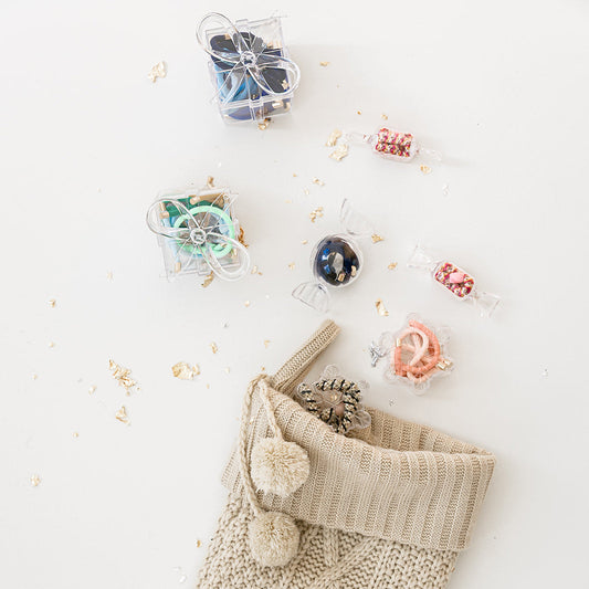 Knitted beige Christmas stocking with pom-poms on a white background with small gift boxes and decorative items.