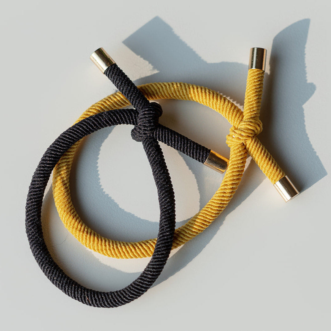 Two hair ties, one black and one mustard yellow, on a light gray background.