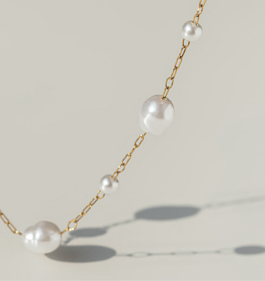 Pearl necklace with gold chain on a light background
