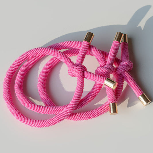 Pink braided hair tie with gold ends on a light gray background