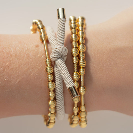 gray hair tie and gold beaded dia bracelets on a wrist against a neutral background