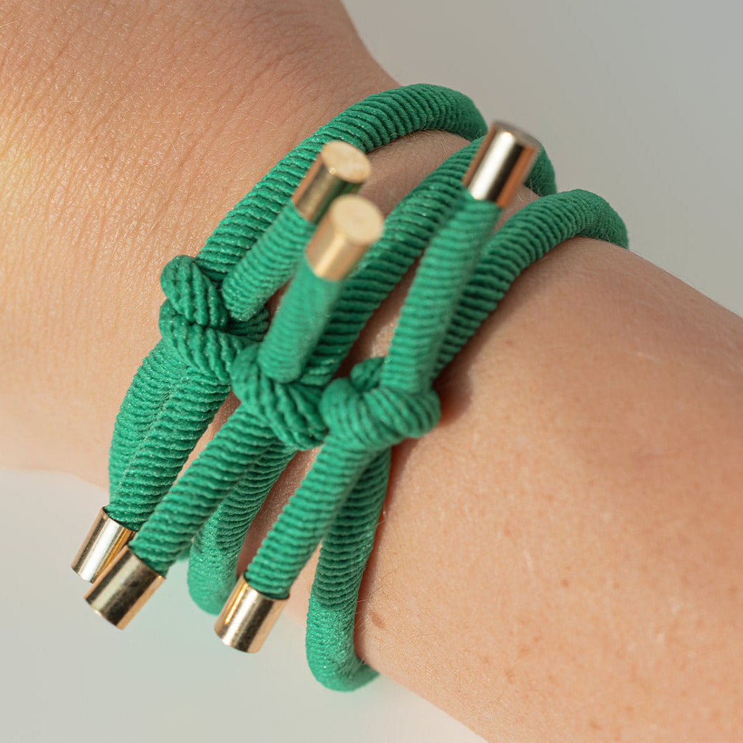Green hair ties with gold accents on a wrist against a neutral background