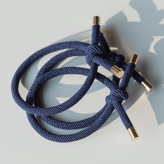 Navy blue hair tie with gold ends on a light gray background