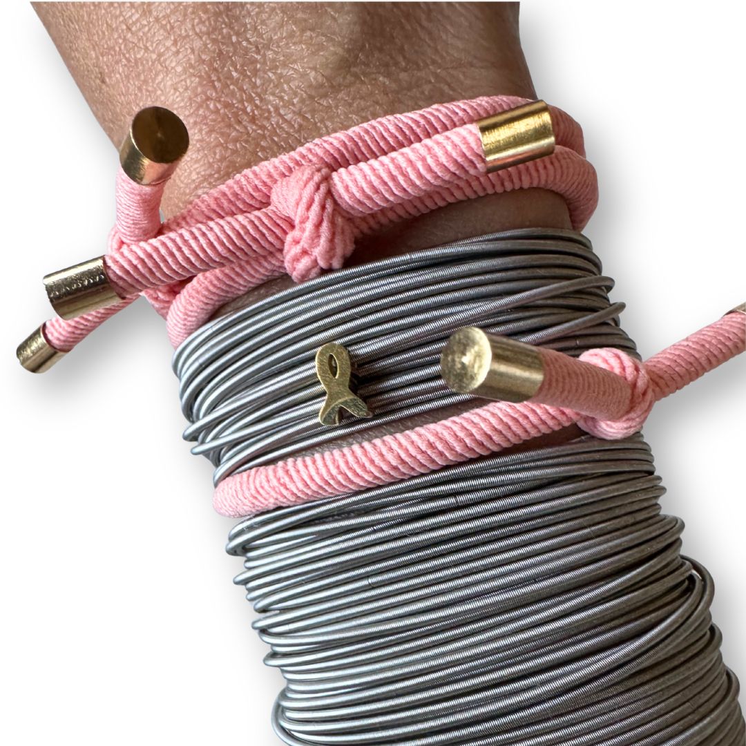 Close-up of hands wearing pink hair tie and stainless steel DIA bracelets with gold ribbon charm on a white background