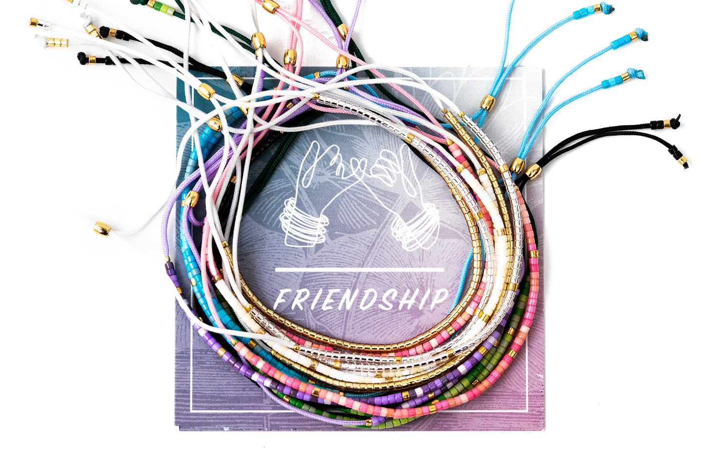 A variety of tiny beaded bracelets on string. Silver,Gold,Pink,purple,blue,green and black. Bracelets are on a card that says friendship.