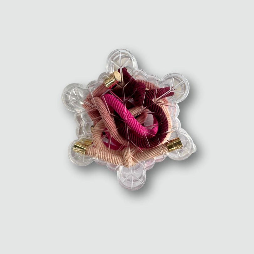 Decorative snowflake packaging hair ties with pink and gold accents on a light gray background