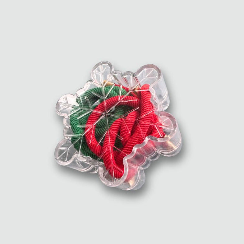 red, green and white hair ties in a plastic snowflake on a clear acrylic base against a light gray background 
