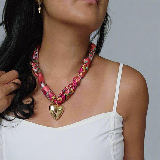 Woman wearing a colorful scarf necklace with a heart pendant on a plain background