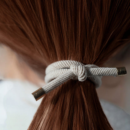 Close-up of brown hair tied with a white hair tie against a blurred background