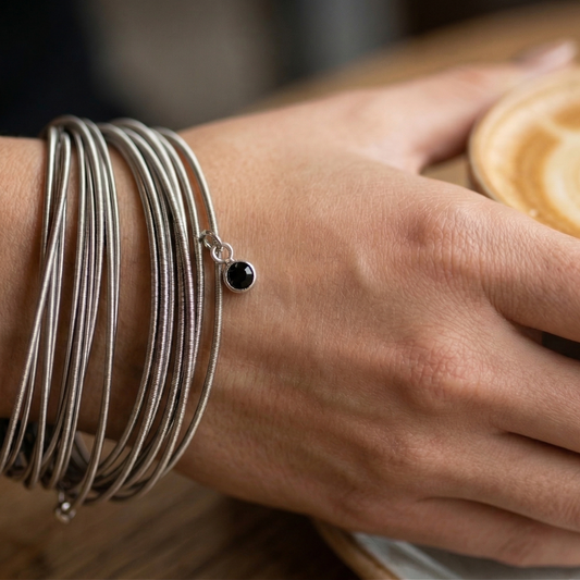 Hand with multiple bracelets holding a cup of coffee. black crystal Charm