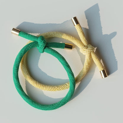 Two braided hair ties, one green and one yellow, on a light gray background.