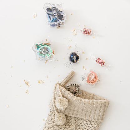 Knitted beige Christmas stocking with pom-poms on a white background with small gift boxes and decorative items.