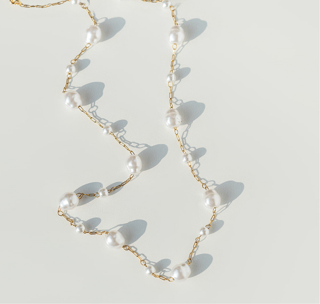 Pearl necklace with gold chain on a light background