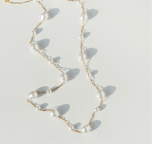 Pearl necklace with gold chain on a light background