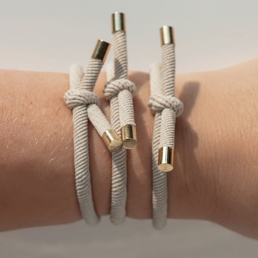 Three beige braided hair tie with gold ends on a wrist against a neutral background