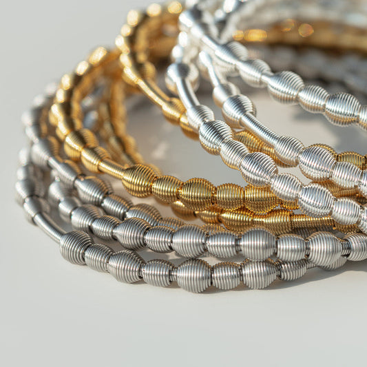 Stack of gold and silver all beaded dia bracelets on a light gray background
