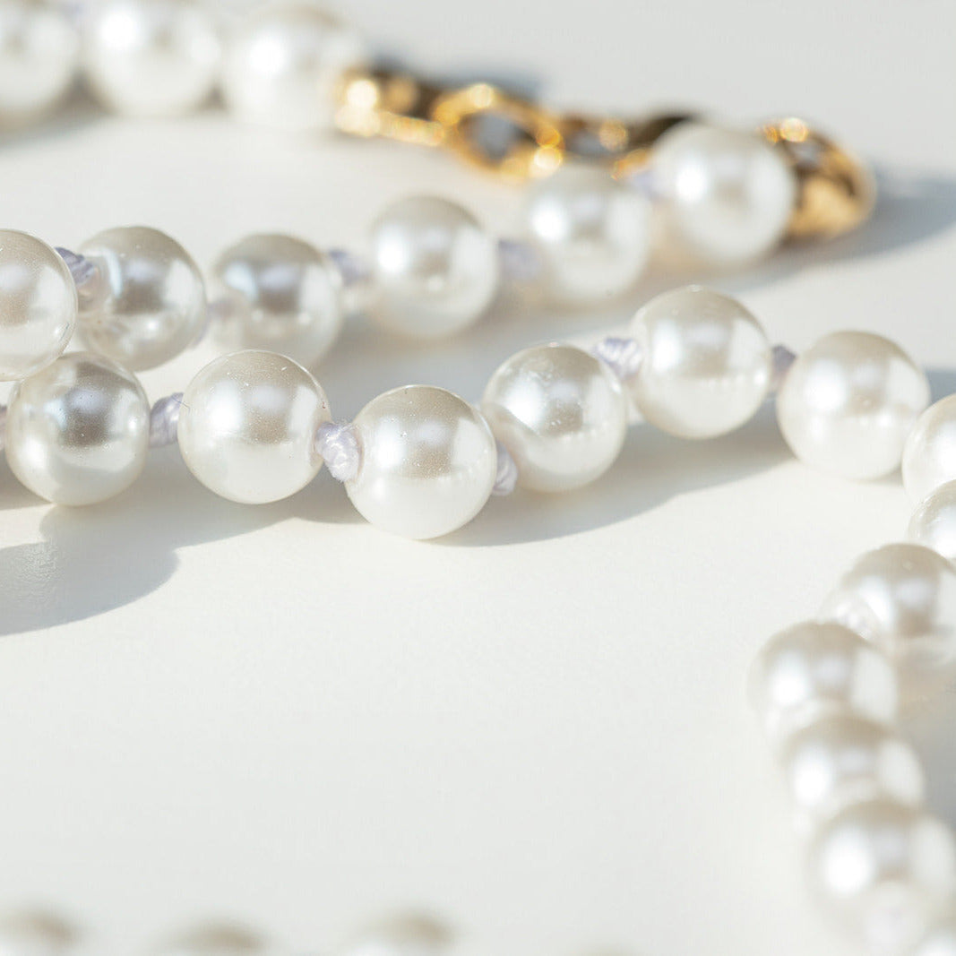 Pearl necklace on a light surface with a gold ring