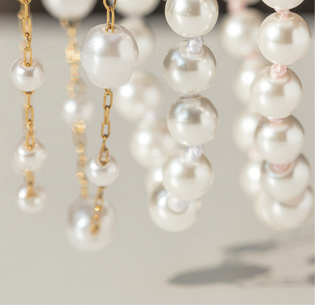 Close-up of pearl earrings with gold chains on a neutral background