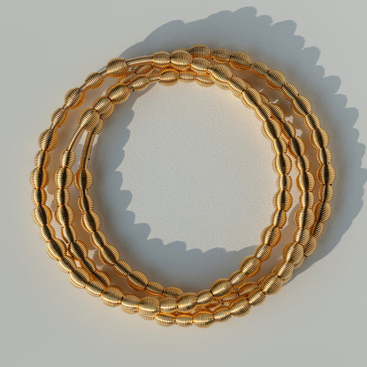 Three gold dia bracelets stacked on a light gray background