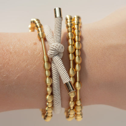  gray hair tie and gold beaded dia bracelets on a wrist against a neutral background