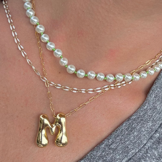 Necklace with a gold 'M' pendant and pearl strands on a person wearing a gray top.