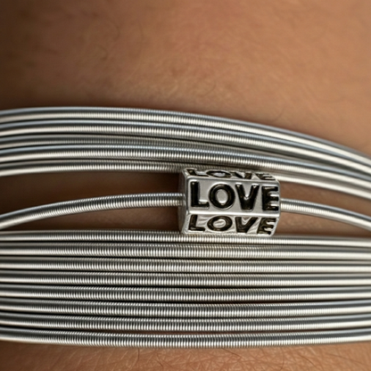 Silver wire bracelet with 'LOVE' charm on a brown leather surface