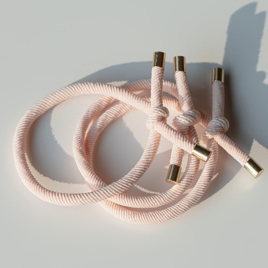 Pink hair tie with gold ends on a light gray background