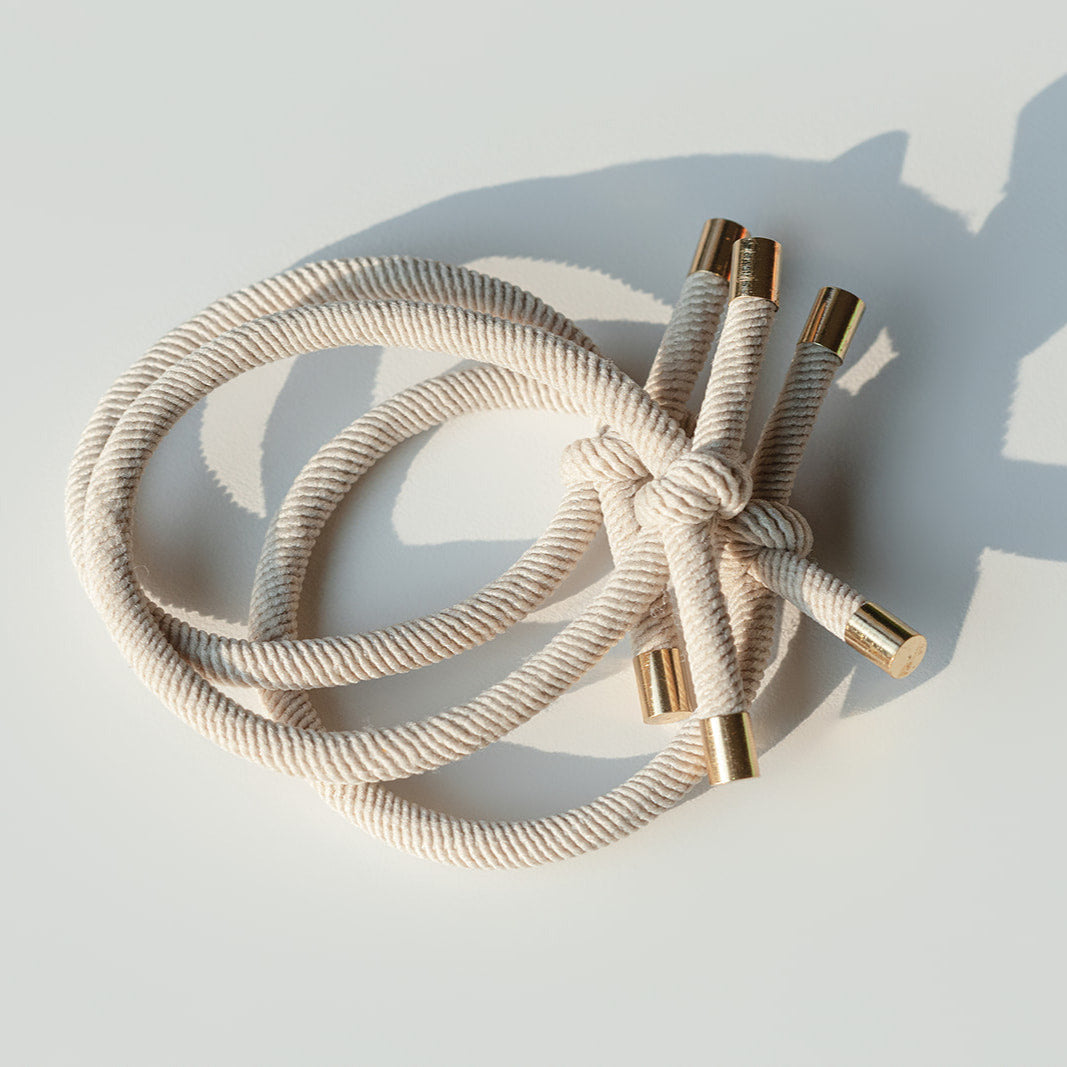 Beige braided hair tie with gold connectors on a light gray background