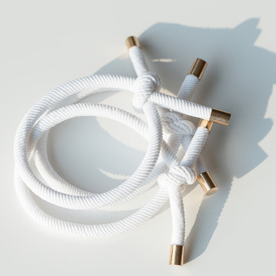 White braided hair tie with gold connectors on a light gray background