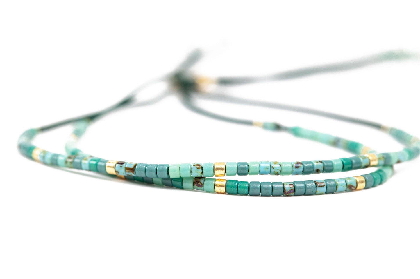 2 tiny beaded bracelets on string. Shades of tiny turquoise beads with a few gold beads throughout.